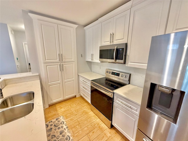 kitchen with light stone counters, stainless steel appliances, sink, light hardwood / wood-style floors, and white cabinetry