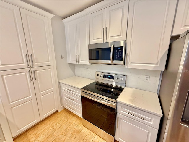 kitchen with light stone countertops, white cabinetry, decorative backsplash, appliances with stainless steel finishes, and light wood-type flooring