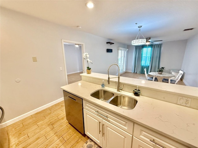 kitchen featuring light stone countertops, stainless steel dishwasher, sink, decorative light fixtures, and light hardwood / wood-style floors