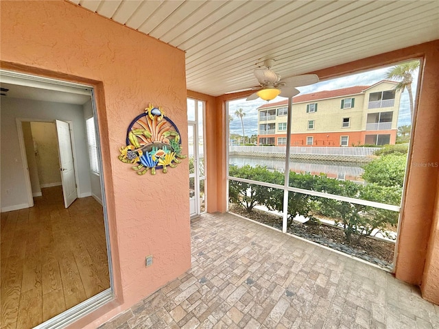 unfurnished sunroom featuring ceiling fan and a water view