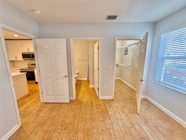 unfurnished bedroom featuring ensuite bath, a spacious closet, light hardwood / wood-style flooring, a textured ceiling, and a closet