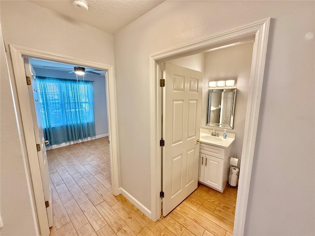 hall with sink, a textured ceiling, and light wood-type flooring