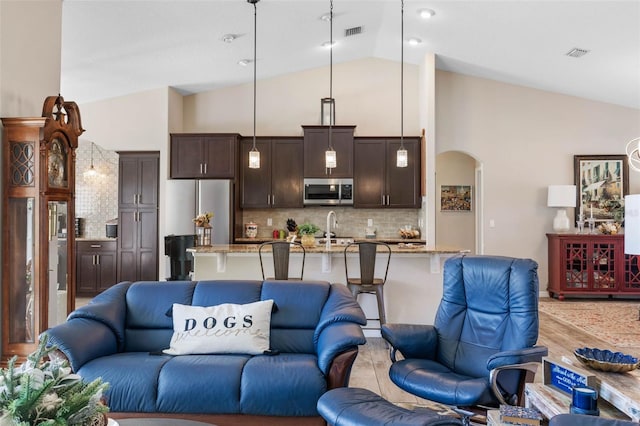 kitchen featuring stainless steel appliances, light stone counters, backsplash, pendant lighting, and dark brown cabinets