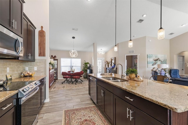 kitchen featuring sink, hanging light fixtures, stainless steel appliances, a center island with sink, and light wood-type flooring