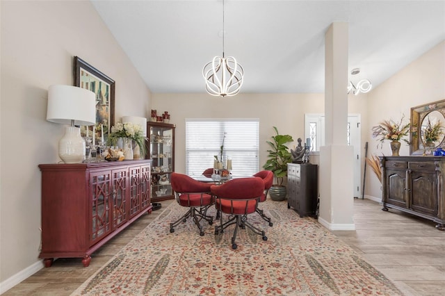 dining area with lofted ceiling, ornate columns, light wood-type flooring, and a chandelier