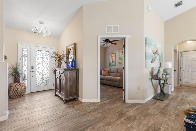 foyer entrance with ceiling fan with notable chandelier, light hardwood / wood-style floors, and high vaulted ceiling