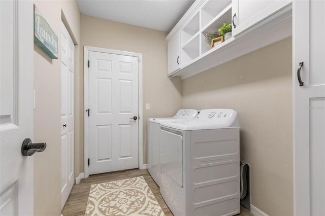 clothes washing area with washer and dryer, cabinets, and light wood-type flooring