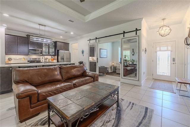 living room featuring a barn door, light tile patterned floors, crown molding, and a chandelier