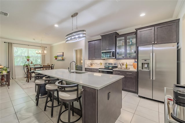 kitchen with pendant lighting, a kitchen island with sink, sink, appliances with stainless steel finishes, and dark brown cabinets