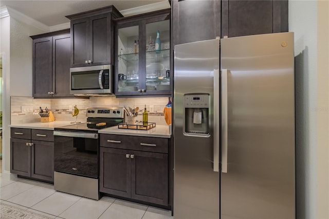 kitchen featuring appliances with stainless steel finishes, backsplash, dark brown cabinetry, crown molding, and light tile patterned floors