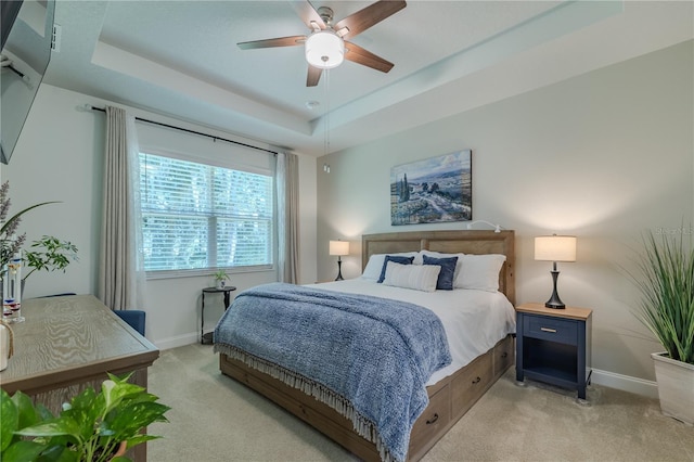 carpeted bedroom with ceiling fan and a raised ceiling