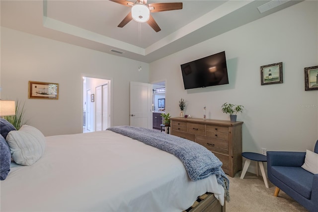 carpeted bedroom featuring a tray ceiling, ceiling fan, and ensuite bathroom