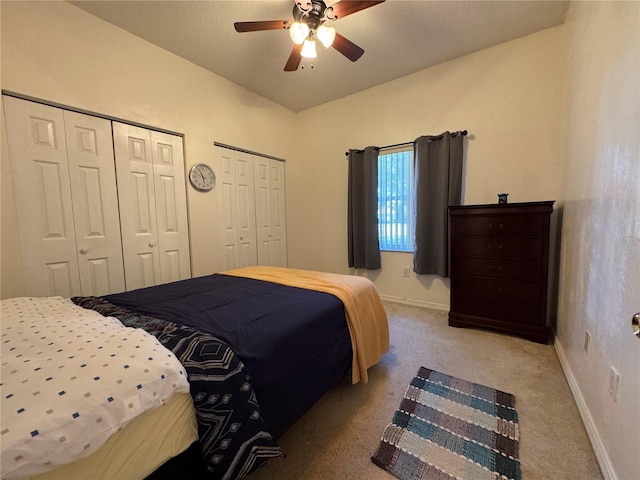 bedroom with ceiling fan, light colored carpet, and two closets