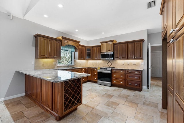 kitchen featuring kitchen peninsula, appliances with stainless steel finishes, backsplash, and light stone countertops