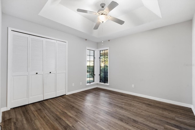 unfurnished bedroom featuring ceiling fan, dark hardwood / wood-style floors, and a tray ceiling