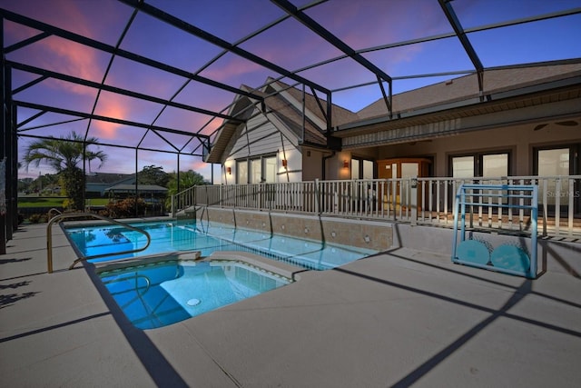 pool at dusk with glass enclosure, an in ground hot tub, and a patio