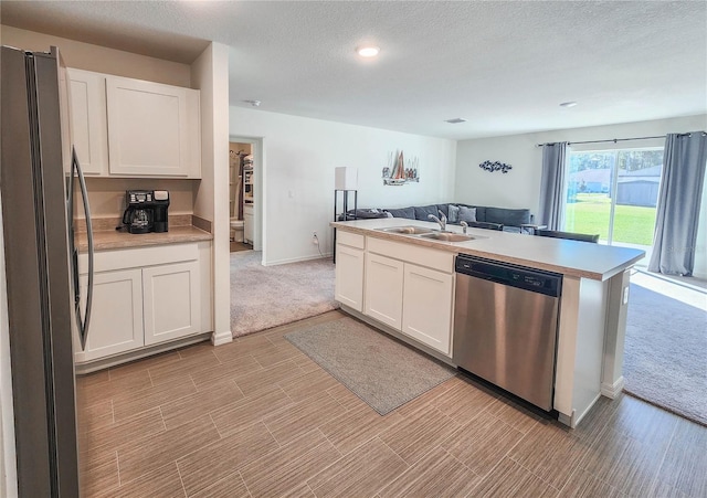 kitchen with appliances with stainless steel finishes, a textured ceiling, light colored carpet, sink, and white cabinetry