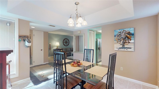 dining space with a tray ceiling, light tile patterned flooring, and a chandelier