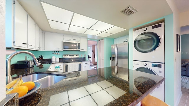 kitchen featuring appliances with stainless steel finishes, stacked washing maching and dryer, dark stone counters, sink, and white cabinetry