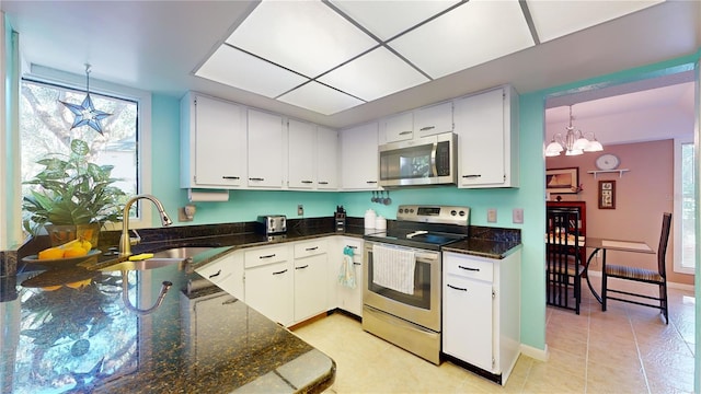 kitchen with appliances with stainless steel finishes, sink, a notable chandelier, white cabinets, and hanging light fixtures