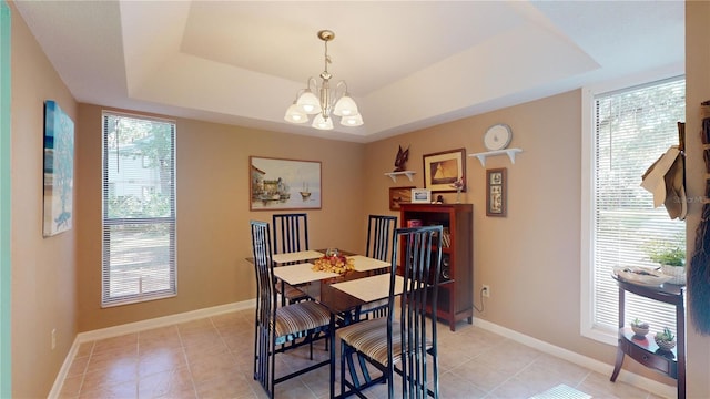 dining room with a tray ceiling, plenty of natural light, light tile patterned floors, and a notable chandelier