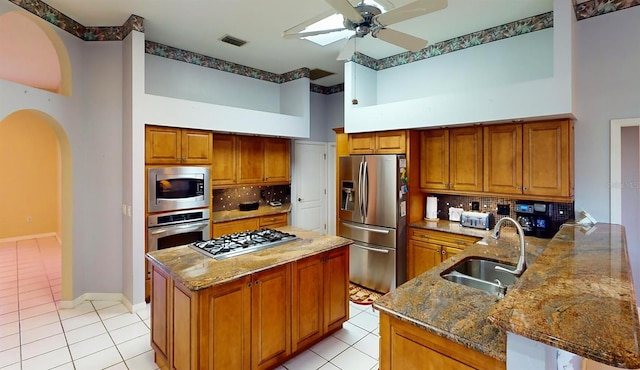 kitchen featuring a high ceiling, a center island with sink, sink, appliances with stainless steel finishes, and tasteful backsplash