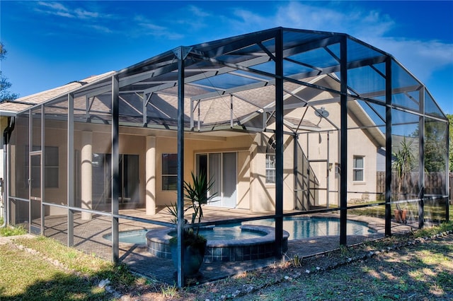 rear view of property featuring a swimming pool with hot tub, a patio, and glass enclosure