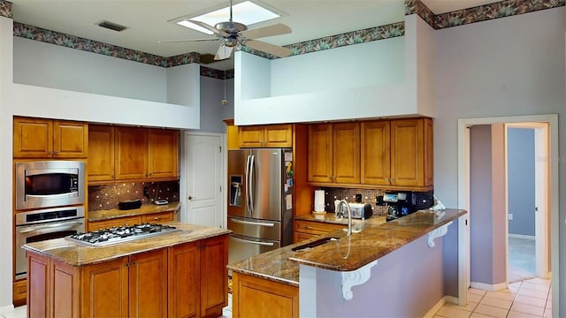 kitchen with kitchen peninsula, appliances with stainless steel finishes, backsplash, sink, and dark stone countertops