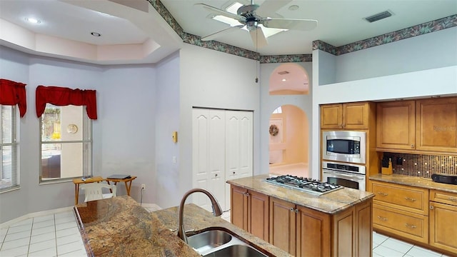 kitchen featuring light stone countertops, stainless steel appliances, ceiling fan, sink, and a center island