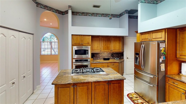 kitchen featuring light stone countertops, a center island, stainless steel appliances, a towering ceiling, and light tile patterned flooring