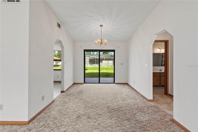 spare room with light colored carpet and an inviting chandelier