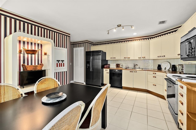 kitchen featuring sink, cream cabinets, decorative backsplash, light tile patterned floors, and black appliances