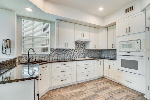 kitchen featuring white appliances, backsplash, dark stone counters, sink, and white cabinetry