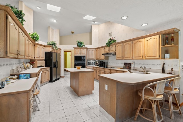 kitchen with kitchen peninsula, sink, black appliances, a kitchen island, and a breakfast bar area