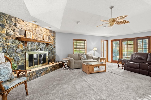 carpeted living room featuring ceiling fan, a stone fireplace, a textured ceiling, and a wealth of natural light