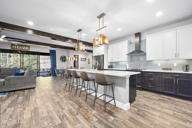 kitchen featuring white cabinets, stainless steel appliances, wall chimney range hood, and light wood-type flooring