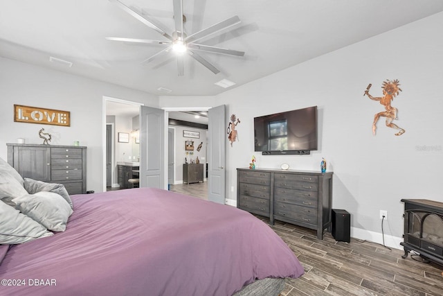 bedroom featuring a wood stove, ceiling fan, ensuite bathroom, and dark hardwood / wood-style floors