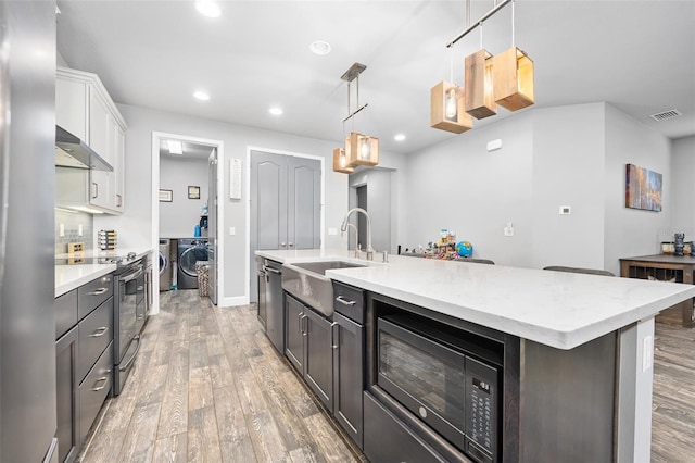 kitchen with washing machine and clothes dryer, white cabinetry, sink, electric range, and a kitchen island with sink