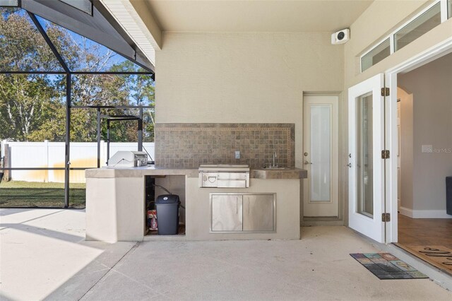 view of patio with an outdoor kitchen, a lanai, and sink