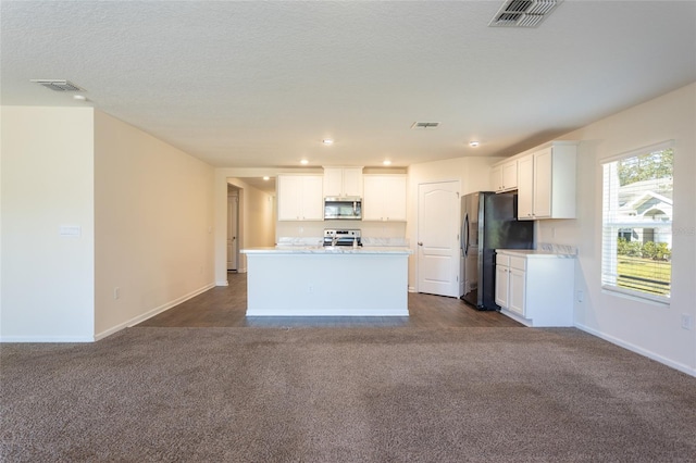 kitchen with appliances with stainless steel finishes, a textured ceiling, dark colored carpet, white cabinetry, and an island with sink