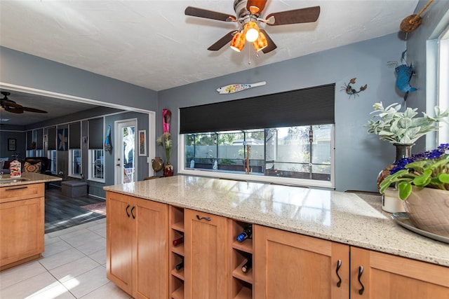 kitchen with light stone counters, sink, light tile patterned flooring, and ceiling fan