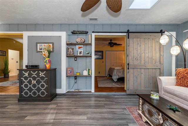 living room with a textured ceiling, a barn door, wood walls, and dark hardwood / wood-style floors