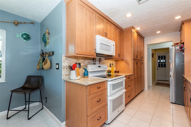 kitchen featuring tasteful backsplash, light stone counters, a textured ceiling, white appliances, and light tile patterned flooring