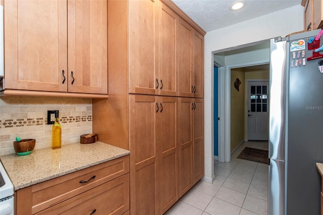 kitchen with light stone countertops, backsplash, a textured ceiling, light tile patterned floors, and stainless steel refrigerator