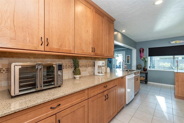 kitchen featuring white dishwasher, sink, light tile patterned floors, tasteful backsplash, and light stone counters