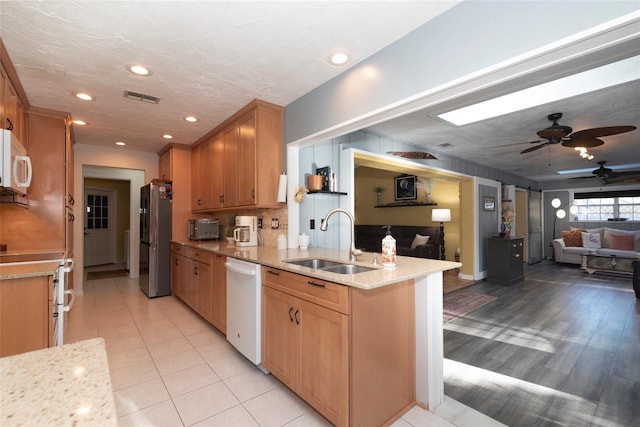 kitchen featuring white appliances, sink, ceiling fan, light stone counters, and kitchen peninsula