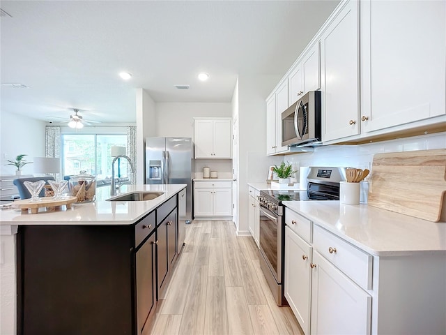 kitchen featuring appliances with stainless steel finishes, light wood-type flooring, sink, white cabinetry, and an island with sink