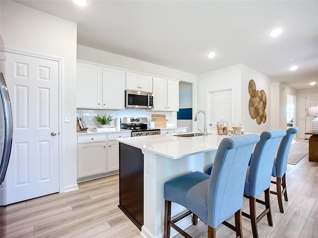 kitchen featuring light hardwood / wood-style floors, white cabinetry, stainless steel appliances, and a kitchen island with sink