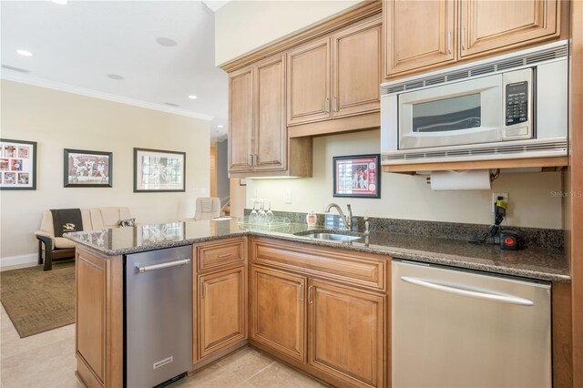 kitchen with sink, kitchen peninsula, dark stone counters, appliances with stainless steel finishes, and ornamental molding