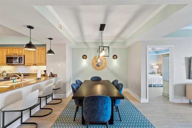 dining room with a textured ceiling, light hardwood / wood-style floors, ornamental molding, and sink